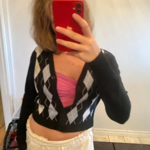 Svart croppad kofta med rutor från SHEIN - Svart croppad kofta från SHEIN med klassiskt argylemönster i ljusblått och vitt. V-ringad med knappar framtill och långa ärmar. Perfekt för dig som gillar preppy vibes och vill ha något snyggt och bekvämt till vardags.