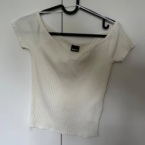 Vit ribbad topp från Gina Tricot - Säljer en vit ribbad topp från Gina Tricot med v-ringning och korta ärmar. Toppen har en figurnära passform och är perfekt för en stilren och enkel look. Oanvänd. 