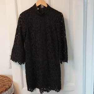 Svart spetsklänning - Elegant svart klänning i spets med trekvartsärm och hög hals. Perfekt för en stilren look med vackra detaljer i spetsmönster. Klänningen har en klassisk och tidlös design.