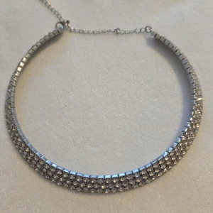 Glittrigt halsband i silver - Snyggt och elegant halsband i silver med flera rader av glittrande stenar. Perfekt för att ge en extra touch av glamour till din outfit. Justerbar kedja för perfekt passform.