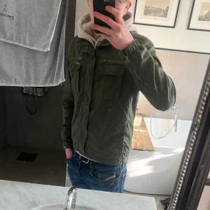 Field jacket grön - Säljer en snygg grön field jacket med dragkedja och knappar. Jackan har flera praktiska fickor och en hög krage. Perfekt för vår och höst! Väldigt sällsynt snygg jacka med hög kvalité. Väldigt true-to-size, men passar även M. Pm vid eventuella frågor