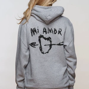 Grå hoodie från Mira Paris - Säljer en grå hoodie från Mira Paris med texten 'Mi Amor' och ett hjärta genomborrat av en pil på ryggen. Hoodien har en klassisk design med känguruficka och justerbar huva. Perfekt för en avslappnad stil.