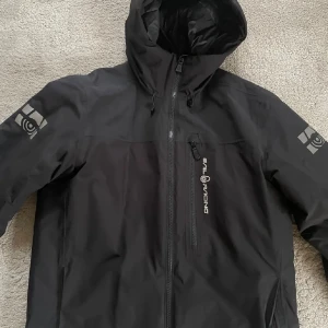 Svart jacka från Sail Racing - Säljer en svart jacka från Sail Racing med huva och dragkedja. Jackan har en stilren design med logotyp på bröstet och ärmarna. Perfekt för kyligare väder. Priset går att diskutera!