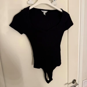 Svart ribbad bodysuit från H&M - Snygg svart ribbad bodysuit med korta ärmar och v-ringning i storlek Xs!