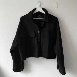 Svart croppad kappa - Snygg svart croppad kappa från Stradivarius med knappar framtill och två stora fickor på bröstet. Jackan har långa ärmar, är i storlek M men är liten i storlek så passar mer XS/S. Nästan inte använd 💘