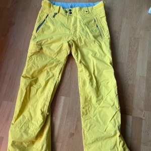 Gula täckbyxor från 686 - Säljer ett par gula täckbyxor från 686. Byxorna har flera praktiska fickor med dragkedja och bälteshällor. Perfekta för vintersport med sitt tåliga material och stilrena design. Passar bra för kalla dagar i backen.