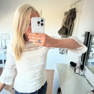 Vit spetsblus - Säljer en elegant vit spetsblus med trekvartsärm och fina spetsdetaljer. Perfekt för en stilren look. Blusen har en rund hals och en knapp i nacken för enkel påklädning.