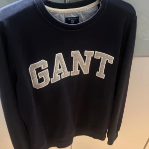 Mörkblå sweatshirt från GANT - Säljer en snygg mörkblå sweatshirt från GANT med stort vitt logotryck på bröstet. Tröjan har långa ärmar och en rund halsringning. 