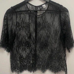 Svart spetsblus från H&M - Säljer en elegant svart spetsblus från H&M. Blusen har korta ärmar och knappar längs ryggen. Perfekt för en stilfull look.