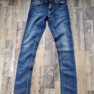 Blå jeans från Nudie Jeans - Snygga blå jeans från Nudie Jeans med klassisk femficksdesign och orange sömmar. De har en smal passform och är tillverkade i slitstarkt denim. Perfekta för en stilren look obs dom är oanvända.