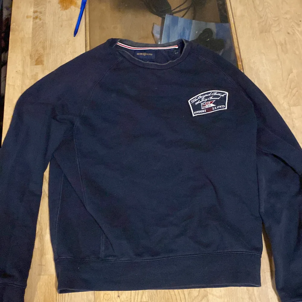 Säljer en mörkblå tröja från Henri Lloyd med ett broderat märke på bröstet. Tröjan har långa ärmar och ribbade muddar vid ärmslut och nederkant. Perfekt för en avslappnad stil.. Neuletakit & Villapaidat.