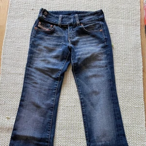 Mörkblå jeans från Diesel - Snygga mörkblå jeans från Diesel med klassisk femficksdesign och dubbla knappar i midjan. Jeansen har en låg midja och är bootcut. Märkesdetaljer syns på den lilla fickan framtill. De är jätte snygga, men tyvärr väldigt små på mig. Väldigt korta på mig som är runt 170. Mått: midjemått: 35cm innerbenslängd:75cm