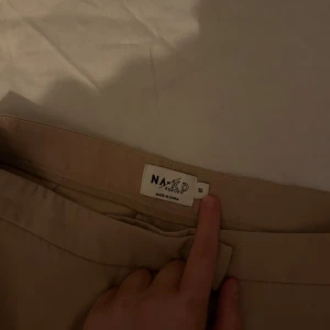 Beige byxor från NA-KD - Snygga beige byxor från NA-KD med en stilren design. Byxorna har en rak passform med slit ner till.