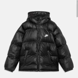 Svart lättvikts dunjacka från Nike - Säljer en svart lättvikts dunjacka från Nike med huva och dragkedja. Jackan har en klassisk pufferdesign med två fickor framtill och en liten Nike-logga på bröstet. Perfekt för kyliga dagar!