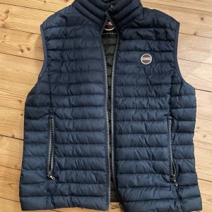 Mörkblå dunväst från Colmar - Snygg mörkblå dunväst från Colmar med dragkedja och quiltad design. Super snygg och bra nu till vår/sommar men även perfekt för lager-på-lager under kyliga dagar. Västen har en stilren look med Colmar-logga på bröstet.  Sparsamt använd!Nypris 2800kr mitt pris 1000kr eller prisförslag vid smidig affär 