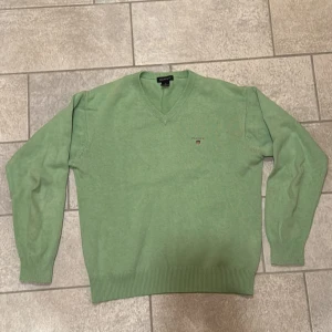 Grön v-ringad tröja från GANT - Säljer en stilren grön v-ringad tröja från GANT. Tröjan har långa ärmar och ribbade muddar vid ärmslut och nederkant. Perfekt för en avslappnad och snygg look.