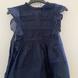 Mörkblå tröja från Holly & Whyte - Säljer en söt mörkblå tröja från Holly & Whyte med volangdetaljer och spets. Tröjan har en luftig passform och är ärmlös, perfekt för varmare dagar. Har använt den 2-3 gånger så är i väldigt bra skick💗