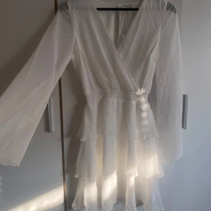 Vit klänning - Säljer en elegant vit chiffongklänning med volanger och v-ringning. Klänningen har långa ärmar och en smickrande omlott-design. Perfekt för sommarens festligheter! Perfekt som studentklänning eller till skolavslutning. Nypris 699kr. Endast testad (lapparna kvar) 