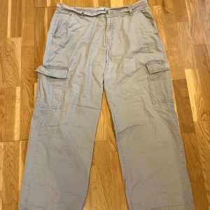 Beige cargobyxor - Säljer ett par beige cargobyxor med flera praktiska fickor och knappstängning. Byxorna har en loose passform och är perfekta för en avslappnad stil. De är sköna att ha på sig och passar till många olika toppar. Det finns ett litet hål på vänster baksida som är väldigt litet, men det tänker ingen på för att det är så litet. 
