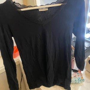 Svart långärmad topp med spets från Cache  - Säljer en svart långärmad topp från  Cache med v-ringning och fina spetsdetaljer längs halsringningen. Perfekt att styla till olika outfits och superenkel att matcha.