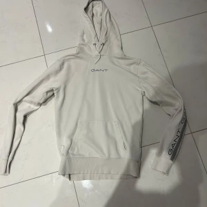 Beige hoodie från GANT - Säljer en stilren beige hoodie från GANT i storlek XS. Tröjan har huva, magficka och GANT-logga på bröstet samt ärmen. Perfekt för en avslappnad och snygg look.