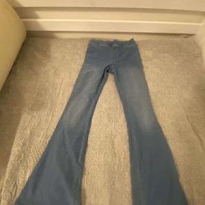 Blå bootcut jeansbyxor - Säljer ett par blå bootcut jeansbyxor med klassisk femficksdesign. Byxorna har utsvängda ben och normal passform i midjan. Perfekta för dig som gillar retrostil och vill ha ett par bekväma jeans till vardags.
