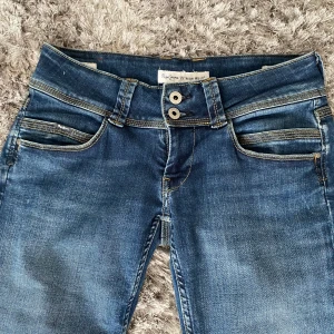 Blå jeans från Pepe - Säljer ett par blå lågmidjade jeans med dubbla knappar i midjan. Storleken är W28 och L34! Byxorna har klassiska fickor fram och ett par fina och unika fickor bak med sömmar. De är i modellen straight. Köpte på plick men har tyvärr inte använts! 💗💗