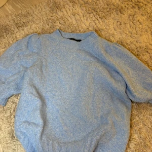 Ljusblå stickad tröja med puffärm - Superfin ljusblå stickad tröja med puffärmar och rund hals. Tröjan har ribbade muddar vid ärmslut och nederkant, vilket ger en snygg passform. Perfekt för kyliga dagar och enkel att styla till olika outfits.