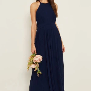 Marinblå långklänning - Marinblå långklänning i halterneck-modell med plisserad kjol och hög halsringning. Klänningen har ärmlös design och markerad midja för en smickrande siluett. Perfekt för bal eller bröllopsgäst/brudtärnor. Jag säljer tre stycken, finns i storlek 10 och 14 (om du tex önskar till fler brudtärnor). Helt oanvända alla tre. Från märket TFNC. 