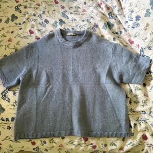 Ljusblå stickad tröja från Gina Tricot - Mysig ljusblå stickad tröja från Gina Tricot med korta ärmar och rund halsringning. Tröjan har en rak passform och ribbade kanter vid ärmslut, hals och nederkant. Använd 1 gång och säljer pågrund av att den är förstor.