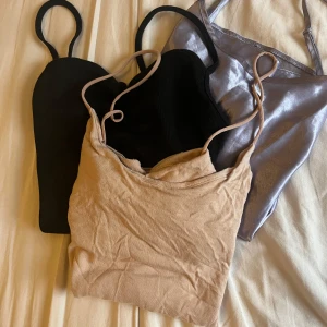 3-pack linnen i olika färger - Säljer tre linnen med smala axelband i svart, beige och glansig silverlila. Alla har en croppad passform och är perfekta till sommaren. Det svarta och beige linnet är i bomull, medan det silverlila är i ett glansigt syntetmaterial.