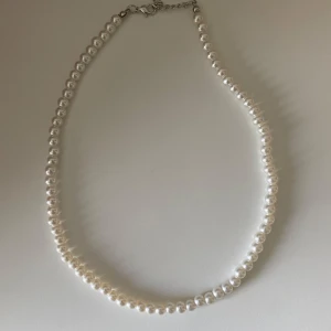 Pärlhalsband med silverfärgat spänne - Klassiskt halsband med vita pärlor och ett justerbart silverfärgat spänne. Perfekt accessoar för att lyfta din outfit med en tidlös och elegant touch.