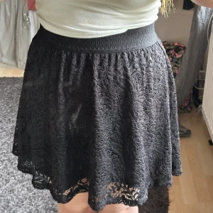 Svart spetskjol med resårmidja - Säljer en svart kjol med vacker spets och bred resår i midjan. Kjolen har en lätt utställd form och är fodrad undertill. Perfekt för dig som gillar feminina detaljer och vill ha något som sticker ut.