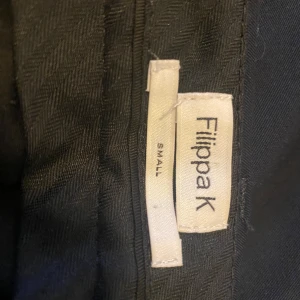 Svarta kostymbyxor från Filippa K - Snygga svarta kostymbyxor från Filippa K i klassisk rak modell. Byxorna har diskreta sidfickor och en bakficka med knapp. Perfekta för en stilren och clean look.🌸