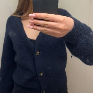 Svart stickad kofta med knappar - Säljer en svart stickad kofta med rund hals och knäppning framtill. Koftan har långa ärmar och en klassisk, enkel design som passar till mycket. Perfekt att slänga på sig när det är lite kyligt.