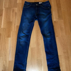 blå jeans tiger of Sweden - Säljer ett par mörkblå jeans i modellen Evolve. Klassisk femficksdesign med normal midja. Jeansen har snygga slitningar och är perfekta till vardags. Storlek 30/32.
