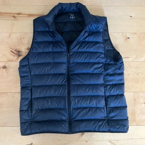 Blå dunväst från Uniqlo - Säljer en stilren blå dunväst från Uniqlo. Västen är ultralätt och har en dragkedja framtill. Perfekt för lager-på-lager under kyliga dagar. 🧥