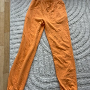 Orange mjukisbyxor med resårmidja - Säljer ett par orange mjukisbyxor med resår i midjan och vid bensluten. Byxorna har en avslappnad passform och är perfekta för en chill stil. Tillverkade i mjukt material för extra komfort.