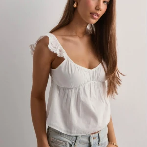 Vit topp från Nelly - Jättesöt topp från Nelly med spetsdetaljer, rosett och djupringning både fram och bak. Prislappen är kvar. Perfekt till sommaren och varmare dagar!🌸