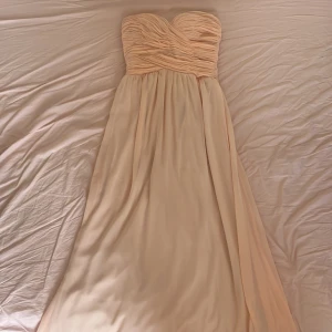 Aprikos rosa långklänning med draperad överdel - Säljer en elegant axelbandslös långklänning  med draperad, hjärtformad överdel och lätt utställd kjol. Perfekt för bal eller fest. Materialet är mjukt och faller snyggt.