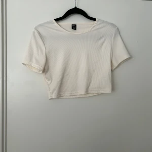 Vit croppad ribbad t-shirt från Gina Tricot - Säljer en enkel och stilren vit croppad t-shirt från Gina Tricot. T-shirten är ribbad och har korta ärmar samt rund halsringning. Perfekt att matcha med jeans eller kjol.