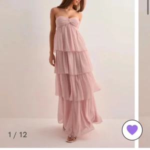 Ljusrosa axelbandslös långklänning med volanger - Romantisk ljusrosa långklänning med flera lager volanger och axelbandslös design. Klänningen har en söt knutdetalj vid bysten och ett luftigt, flowy fall. Perfekt för sommarens speciella tillfällen. Klänningen är aldrig använd, skriv för fler bilder och pris går självklart alltid att diskutera.