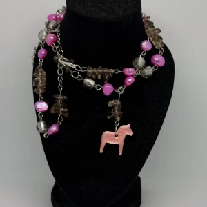 Halsband rosa dalahäst  - 🌟 Unikt handgjort halsband – Dalahäst & pärlor 🌟 Letar du efter ett smycke med personlighet och attityd?  Det här unika halsbandet är en riktig blickfångare! Med en härlig mix av glansiga cerise pärlor, rökiga stenar och silverfärgade detaljer, får du ett smycke som sticker ut i mängden. Den lilla rosa Dalahästen ger en charmig och lekfull touch – en hyllning till tradition med modern twist.  ✨ Perfekt till både vardag och fest ✨ Nickelfritt ✨ Endast ett exemplar – du bär något ingen annan har!