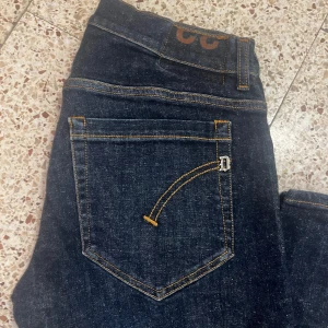 Mörkblå jeansbyxor med kontrastsömmar - Säljer ett par mörkblå jeans med klassisk femficksdesign och snygga kontrastsömmar i gult. Byxorna har normal passform och raka ben. Perfekta till vardags för en stilren look.