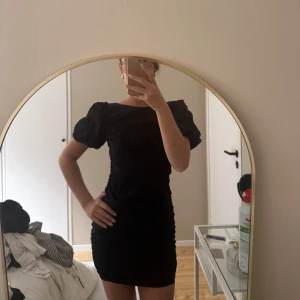 Svart kort puffärmad klänning - Säljer en svart kort klänning med puffärmar och öppen rygg. Klänningen har en tight passform och är perfekt för dig som gillar en stilren look med lite edge.