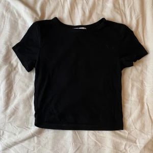 Svart magtröja  - En enkel svart croppad t-shirt från Zara med rund halsringning och korta ärmar. Perfekt att matcha med jeans eller kjol för en stilren look.