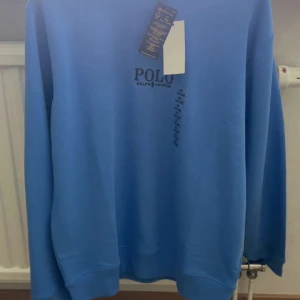 Blå sweatshirt från Polo Ralph Lauren - Snygg blå sweatshirt från Polo Ralph Lauren i klassisk modell med rund hals och tryckt logga på bröstet. Tröjan är tillverkad i mjuk bomullsblandning och har långa ärmar samt ribbade muddar vid ärmslut och nederkant. Perfekt för en chill och stilren look. Alla pris lappar är kvar om du har några funderingar bara hör av dig 😊 