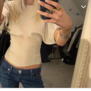 Figursydd topp Zara - Säljer en beige figursydd topp med breda, korta ärmar och rund halsringning. Toppen har en figurnära passform och är sydd i ett mjukt material som ger en clean och stilren look. Perfekt att matcha med jeans för en trendig outfit.
