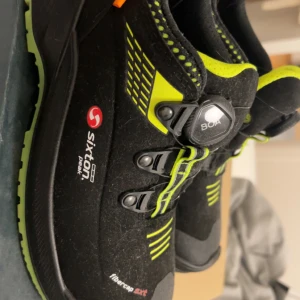 Svarta och neongula arbetsskor från Sixton - Säljer ett par svarta arbetsskor från Sixton med neongula detaljer och BOA-snörning. Skorna har robust sula med bra grepp och är designade för att vara slitstarka och bekväma under långa arbetsdagar. Perfekta för dig som vill ha både stil och funktion.