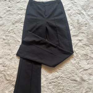 Svarta kostymbyxor från Gina Tricot XS - Snygga svarta kostymbyxor från Gina Tricot i storlek XS. Byxorna har hög midja, utsvängda ben och pressveck framtill. Använda en gång!